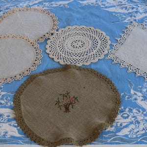 May include: Five crocheted doilies in various sizes and patterns, including a round doily with a floral design, on a blue and white floral tablecloth.