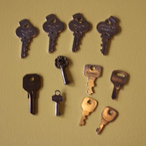 May include: A collection of various metal keys, including skeleton keys and standard door keys, arranged on a yellow background. The keys vary in size, shape, and color, with some showing signs of age and wear.
