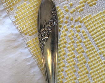 May include: Close-up of a vintage silver spoon with floral detailing. The spoon's handle features an embossed floral design. The spoon is set against a yellow and white patterned background, suggesting a focus on antique silverware or vintage kitchenware.