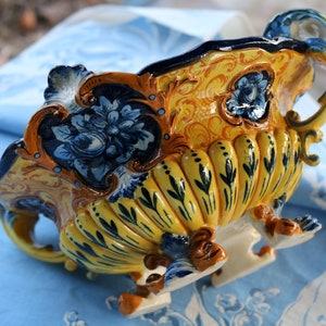 Puede incluir: Un cuenco de cerámica amarillo y azul con intrincados diseños florales y un borde festoneado. El cuenco tiene tres patas y un asa en un lado.