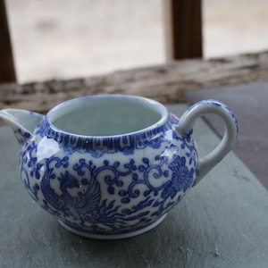 May include: A small, white porcelain teapot with a blue and white floral design. The teapot has a spout and a handle.