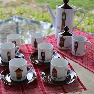 Puede incluir: Un juego de siete tazas y platillos de té de porcelana blanca con diseños de reloj marrones. Las tazas y los platillos tienen un borde marrón. El juego también incluye una tetera y un azucarero de porcelana blanca con diseños de reloj marrones.