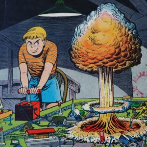 May include: A comic book illustration of a young boy playing with a toy model train set. The boy is holding a detonator, and a mushroom cloud is exploding in the background. The text on the box reads "Junior Kem-Kit for the budding scientist. Educational Happiness."