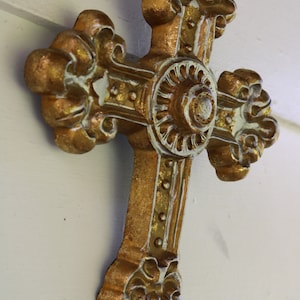May include: An ornate gold and white cross with a decorative centrepiece. The cross is made of metal and has a distressed finish.