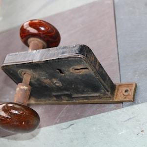 以下が含まれることがあります： 茶色のセラミック製のノブと黒い金属製のプレートが付いた、ヴィンテージのドアノブと錠前のセット。錠前は鍵穴とネジ付きの金属プレートを持っています。