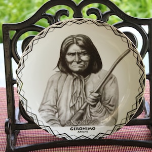 Op de afbeelding: Een wit keramiek bord met een zwart-wit portret van Geronimo, een Apache-leider, die een staf vasthoudt. Het bord heeft een zwart-wit geometrische rand en de tekst "Geronimo Apache" onderaan.