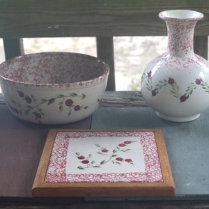 Peut inclure: Ensemble de trois articles de cuisine en céramique blanche avec un glaçage moucheté rose et rouge et un motif floral peint à la main avec des feuilles vertes et des baies rouges. L'ensemble comprend un bol, un vase et une tuile carrée.