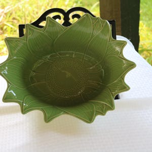 May include: A green ceramic bowl shaped like a sunflower. The bowl has a textured surface and a deep center.