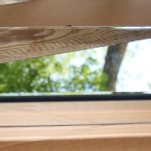 May include: A rectangular mirrored box with a wooden lid. The lid is angled, with a section of wood grain and a mirrored surface reflecting a green and white outdoor scene. The box has a black trim.