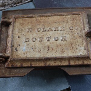 May include: Rectangular, antique metal plate with the embossed text "H N CLARK CO BOSTON". The plate has a hinged door and a rusty, aged appearance, suggesting it is vintage or reclaimed.