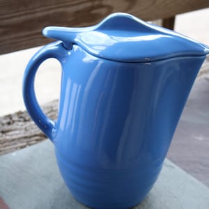 May include: A blue ceramic jug with a lid. The jug has a rounded body and a handle. The lid has a curved shape.