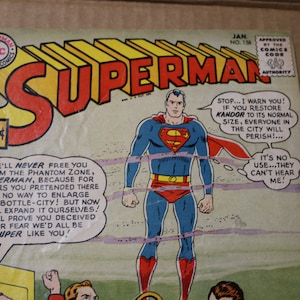 May include: A vintage Superman comic book cover featuring Superman in his red and blue costume, standing with his arms at his sides. The cover text reads "Superman" in large red letters and "We'll never free you from the Phantom Zone, Superman, because for years you pretended there was no way to enlarge our bottle-city! But now we'll expand it ourselves! We'll prove you deceived us for fear we'd all be super like you!" and "Stop... I warn you! If you restore Kandor to its normal size, everyone in the city will perish! ... It's no use...they can't hear me!"