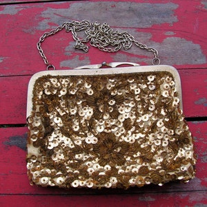May include: A gold sequined evening bag with a chain strap. The bag is closed and has a floral design.