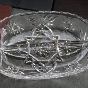 May include: Clear, oval glass serving dish with starburst and geometric patterns. The dish is divided into three sections and has handles. A decorative piece for serving snacks or appetizers.