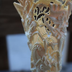 May include: A white carved sculpture of a mythical creature with intricate details. The sculpture is made of bone or ivory and has a delicate, lacy appearance.