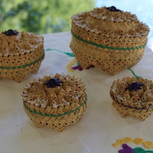 May include: Four woven baskets with lids, decorated with colorful beads and a star-shaped top. The baskets are made of natural materials and have a rustic, handcrafted look.