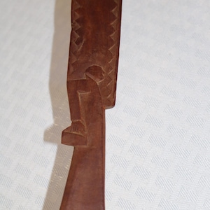 May include: A wooden spoon with a carved figure of a person on the handle. The spoon is brown and has a smooth surface. The figure is carved in detail and has a simple design.