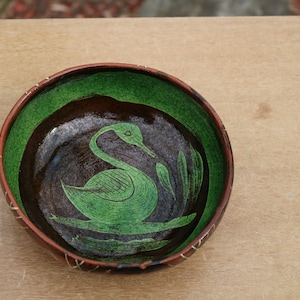 May include: A brown ceramic bowl with a green glaze and a stylized swan design. The bowl has a brown rim and a dark brown interior.