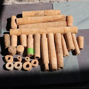 Puede incluir: Una colección de varios componentes de caña de pescar de corcho, incluyendo mangos, empuñaduras y anillos. Las piezas son en tonos marrón claro y beige, algunas mostrando signos de desgaste. Los artículos están dispuestos sobre una superficie gris oscuro, con sombras.