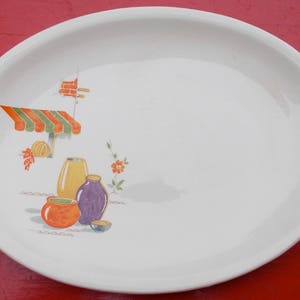 Puede incluir: Plato de servir ovalado blanco con borde dorado y un diseño colorido de un toldo a rayas, flores y jarrones.