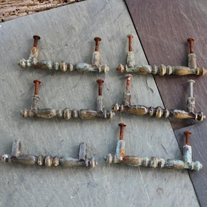 May include: A collection of seven antique bronze drawer pulls with a weathered, aged appearance. Each pull features a series of small, rounded beads and a rusty, cylindrical post. The pulls have a patina of green and blue hues, suggesting exposure to the elements.