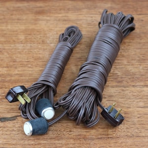 Puede incluir: Dos carretes de cable eléctrico marrón con enchufes e interruptores. Los cables están enrollados y listos para usar.