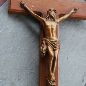 Puede incluir: Un crucifijo de madera con una figura de Jesucristo de color bronce. La cruz es de madera marrón oscuro, y la figura está detallada con una tela drapeada alrededor de la cintura. El fondo es una superficie gris.
