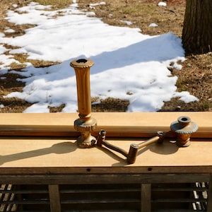 Op de afbeelding: Twee antieke messing kandelaars met een decoratief ontwerp. De kandelaars staan op een houten tafel met een lattenbodem.