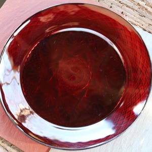 May include: A deep red glass plate with a diamond pattern. The plate is clear and reflects light.