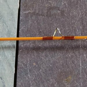 K&ouml;nnte beinhalten: Eine Angelrute aus Holz mit brauner und goldener Oberfl&auml;che. Die Rute ist etwa 1,8 Meter lang und hat eine goldene Spitze.