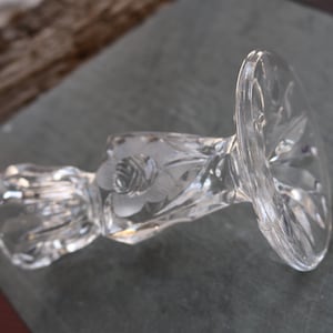 May include: A clear glass candle holder with a floral design. The holder has a wide base and a narrow neck.