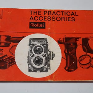 May include: A red and white pamphlet with the title "The Practical Accessories Rollei" and a black and white image of a Rolleiflex camera.
