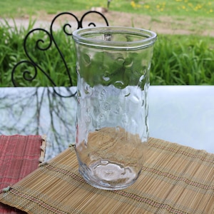 Könnte beinhalten: Eine klare Glasvase mit einer strukturierten, geblähten Oberfläche. Die Vase steht auf einer geflochtenen Bambusmatte.