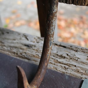 May include: A rusty metal hook with a sharp point, hanging from a wooden beam. The hook is weathered and has a dark brown colour.