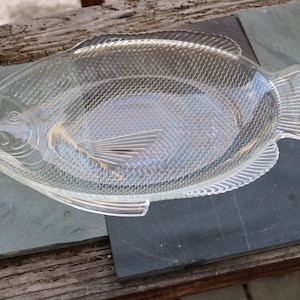 Könnte beinhalten: Eine klare, fischförmige Servierplatte aus Glas mit einer strukturierten Oberfläche. Die Platte ist so gestaltet, dass sie einem Fisch mit Schuppen und Flossen ähnelt.