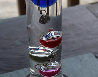 Termómetro Galileo de los 90 con burbujas de vidrio y etiquetas plateadas de colores.