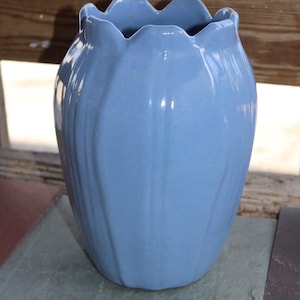Puede incluir: Un jarrón de cerámica azul claro con un borde festoneado y un diseño texturizado y acanalado. El jarrón está vacío y tiene un acabado brillante.