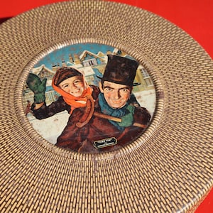 May include: A round, woven, brown and tan tin box with a circular image of a man and a child in winter clothing. The image is set against a snowy background with houses in the distance. The text "Jim Tim" is printed on the box.