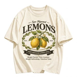 May include: Cream-colored t-shirt featuring a vintage-style graphic of lemons. The design includes the word "LEMONS" above a branch with two lemons, surrounded by a laurel wreath. Text includes "Sun-Ripened", "EST. 2024", and "MEDITERRANEAN SUMMER OOLD".