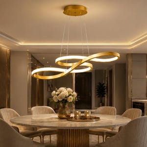 Pode incluir: Um lustre LED com acabamento dourado apresentando dois anéis fluidos em forma de infinito interconectados, suspensos por fios finos a partir de um suporte circular no teto. A luminária emite um brilho quente das bordas internas dos anéis.