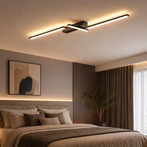 May include: Contemporary black and gold ceiling light with integrated LED lights. The light is mounted on a white ceiling, illuminating a bedroom with a bed, artwork, and a window.
