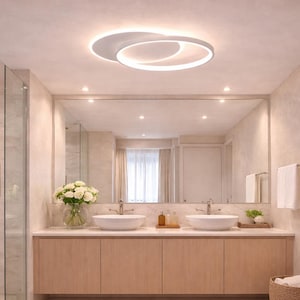 May include: Modern bathroom with a large mirror, two white vessel sinks, and a light wood vanity. A white, circular ceiling light illuminates the space. The walls are a light beige color, and a shower is visible on the left.