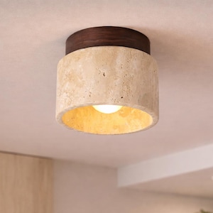 Könnte beinhalten: Eine moderne Deckenleuchte mit einem zylindrischen, strukturierten beigefarbenen Schirm und einer dunkelbraunen Oberseite. Das Licht strahlt warm. Die Leuchte ist an einer weißen Decke montiert und zeigt ein minimalistisches Design.