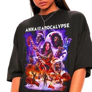 Könnte beinhalten: Schwarzes T-Shirt mit einer farbenfrohen Grafik aus dem Film "Anna and the Apocalypse". Das Design zeigt verschiedene Charaktere und den Filmtitel in Weiß. Das T-Shirt wird getragen.