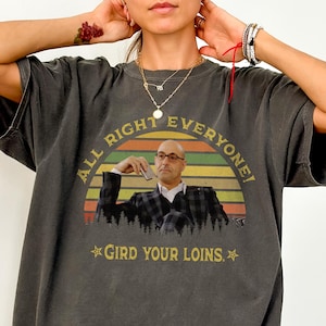 Puede incluir: Camiseta gris oscuro con el texto "ALL RIGHT EVERYONE!" sobre una imagen de un hombre con traje, y "GIRD YOUR LOINS." debajo. La camiseta es de talla grande y tiene un aspecto vintage.