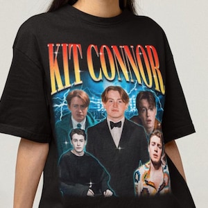 May include: A black short-sleeve t-shirt featuring a graphic print of Kit Connor. The design includes the text KIT CONNOR in a yellow-to-red gradient font above multiple photographic portraits of the actor set against a blue lightning background.