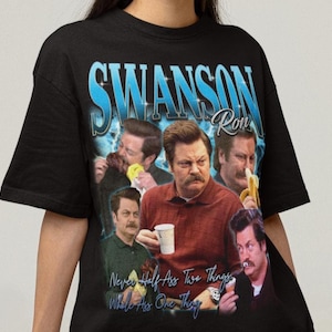 May include: A black short-sleeve t-shirt featuring a graphic print of Ron Swanson in various poses. The text reads SWANSON Ron at the top and Never Half Ass Two Things, Whole Ass One Thing at the bottom in a blue font with a lightning background.