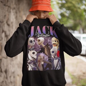 May include: Black sweatshirt featuring a graphic of Jack Skellington from The Nightmare Before Christmas. The design includes the text "JACK Skellington" in a gradient font, with multiple images of Jack's face.