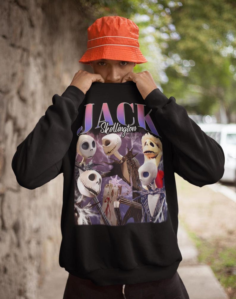 May include: Black sweatshirt featuring a graphic of Jack Skellington from The Nightmare Before Christmas. The design includes the text "JACK Skellington" in a gradient font, with multiple images of Jack's face.