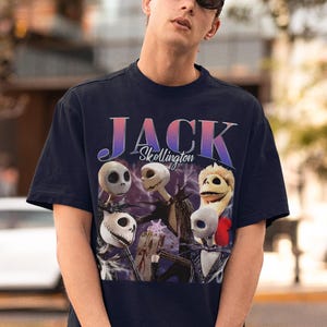 May include: Navy blue t-shirt featuring a graphic of Jack Skellington from The Nightmare Before Christmas. The design includes the text "JACK Skellington" in a gradient font, and images of Jack's face.